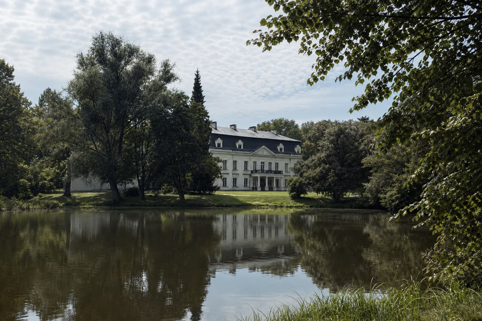 Historyczna rezydencja nad stawem, otoczona starymi drzewami